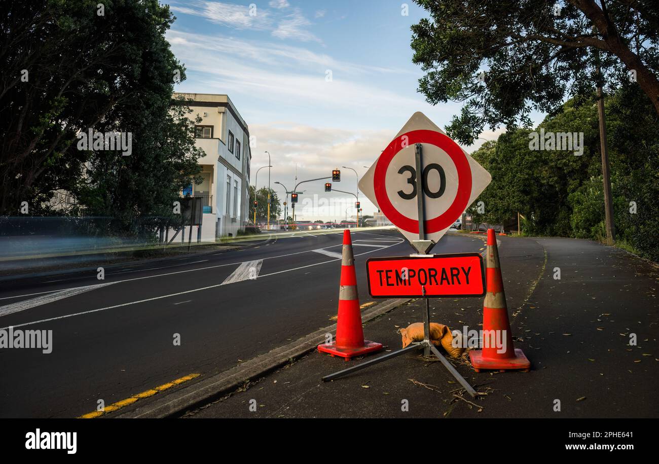 Temporäres Schild mit 30km Geschwindigkeitsbegrenzung und Verkehrskegel am Straßenrand. Autolichtspuren auf der Straße. Auckland. Stockfoto