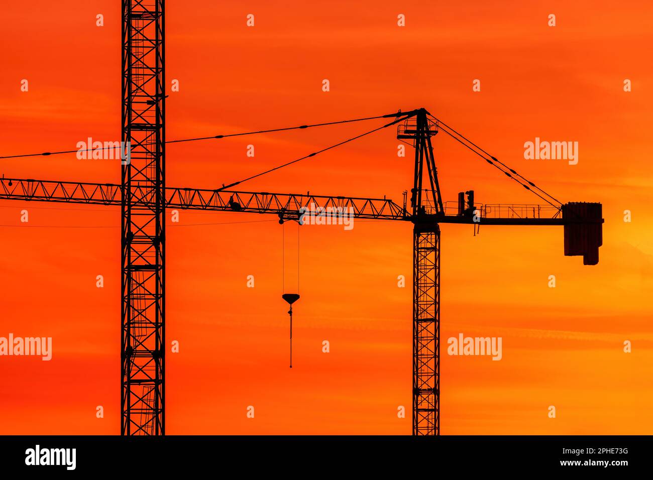 Silhouette von Baukränen vor dem leuchtend orangefarbenen Sonnenuntergangshimmel, Industriemaschinen und technischen Geräten Stockfoto
