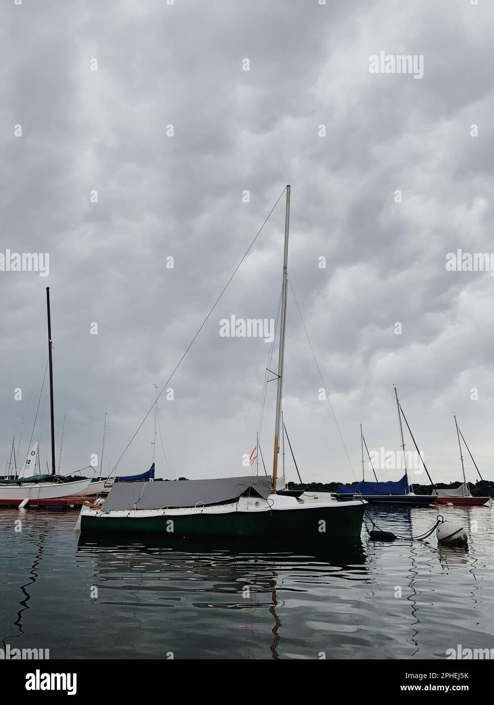 Eine Gruppe kleiner Segelboote wird auf einem See, der von einem wolkigen Himmel umgeben ist, schwimmend gesehen Stockfoto