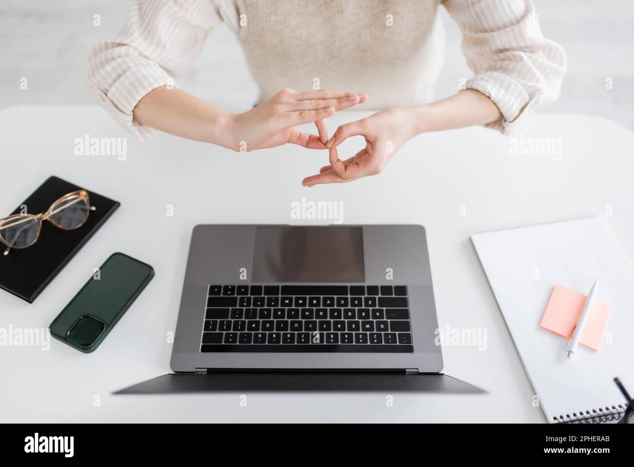 Zugeschnittene Ansicht des Lehrers mit Dolmetschschild auf Körpersprache in der Nähe von Laptop und Smartphone auf dem Schreibtisch, Stockbild Stockfoto