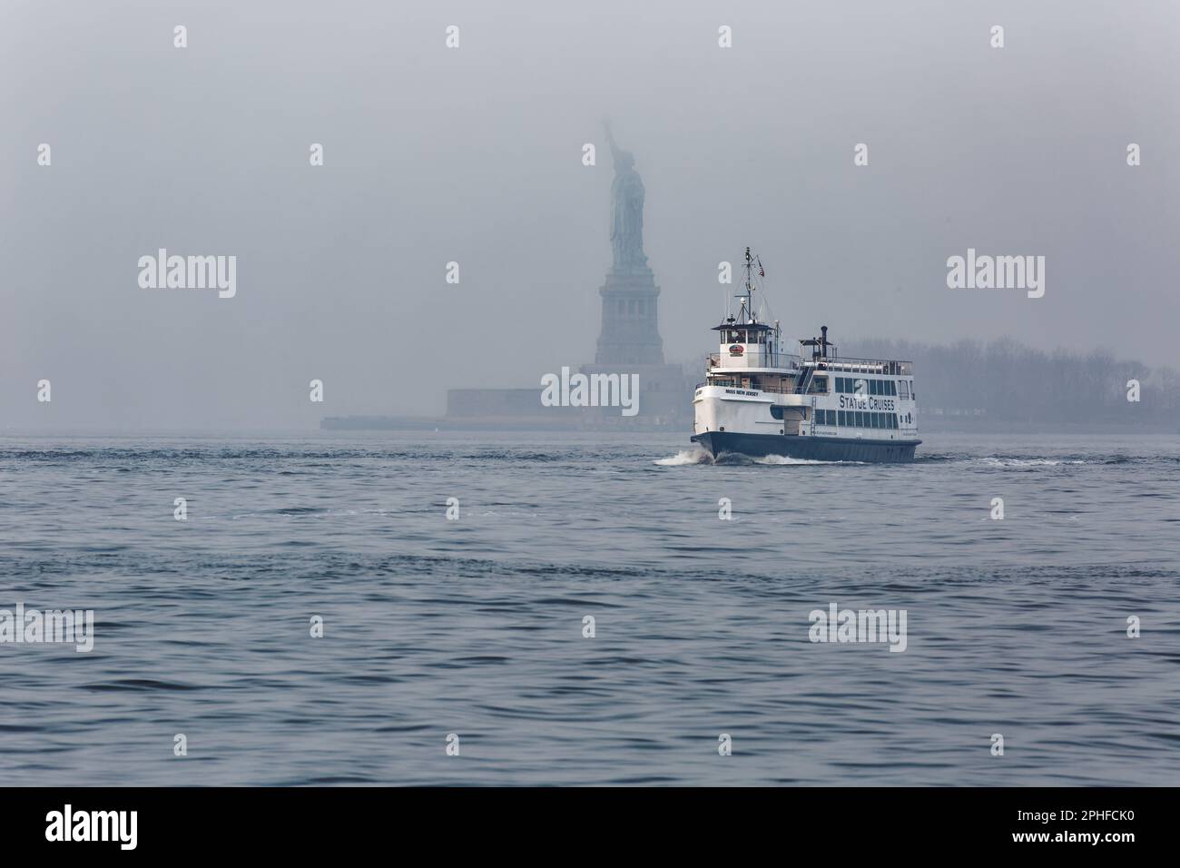 Pendler und Touristen sehen die Freiheitsstatue von Fähren und Tourbooten im Hafen von New York an einem nebeligen Februar-Morgen. Stockfoto