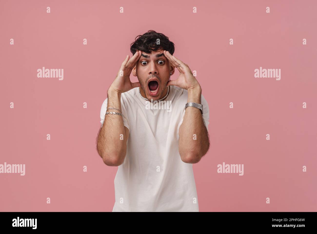 Porträt eines jungen, attraktiven, geschossenen Mannes mit weit geöffneten Augen und Mund, der seinen Kopf mit beiden Händen berührt und nach unten schaut, während er in der Liebe steht Stockfoto