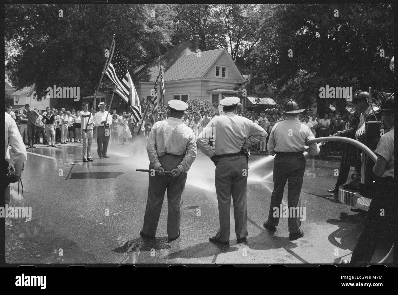 Männer, die amerikanische Flaggen halten, um gegen die Integration der Central High School zu protestieren, stehen auf der Straße, während andere zusehen und die Polizei besprüht sie mit Wasser aus dem Schlauch, Little Rock, AR, 8/20/1959. (Foto: John T Bledsoe/US News & World Report Magazine Fotosammlung Stockfoto