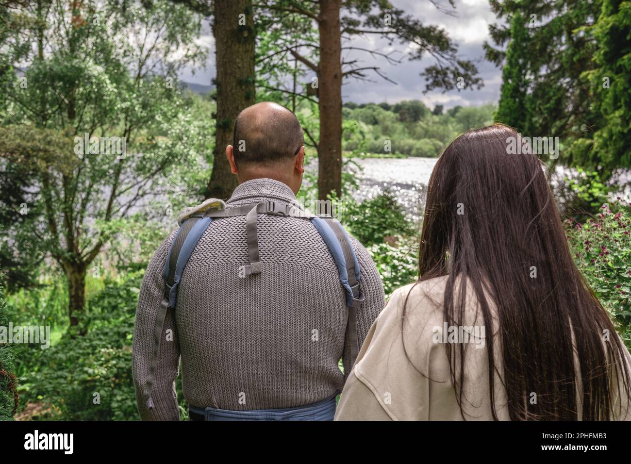 Foto von den Hintern von zwei Eltern, die im Frühling im Dr. Neil's Garden in Edinburgh in der Natur spazieren. Der Vater trägt eine Babytragetasche. Mull Stockfoto