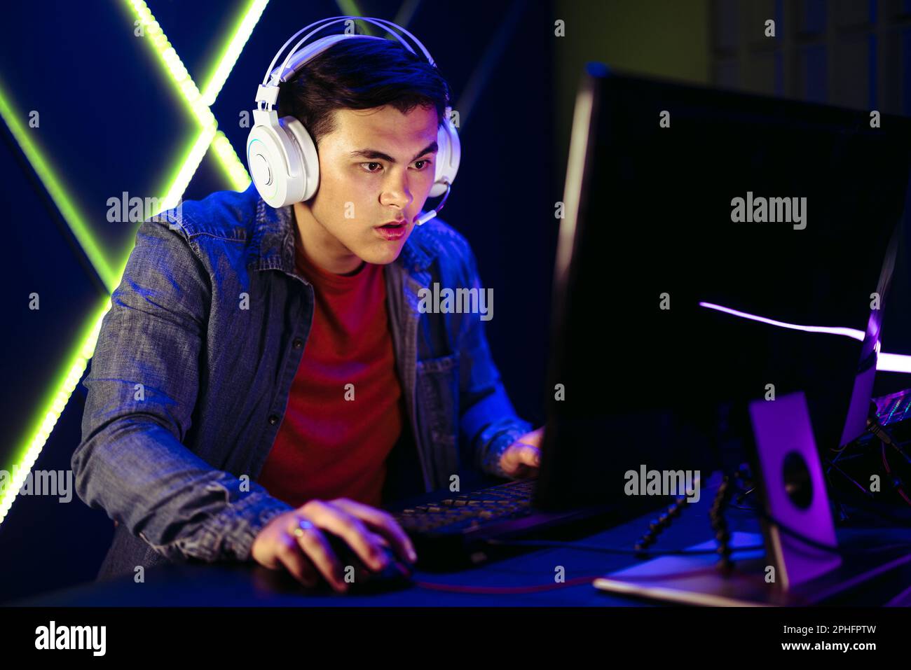 Junger Mann, der sich auf den Computerbildschirm konzentriert, während er ein Online-Videospiel spielt. Mit seiner Blase auf den bewegten Bildern und der Hand, die die Maus greift, ist er es Stockfoto