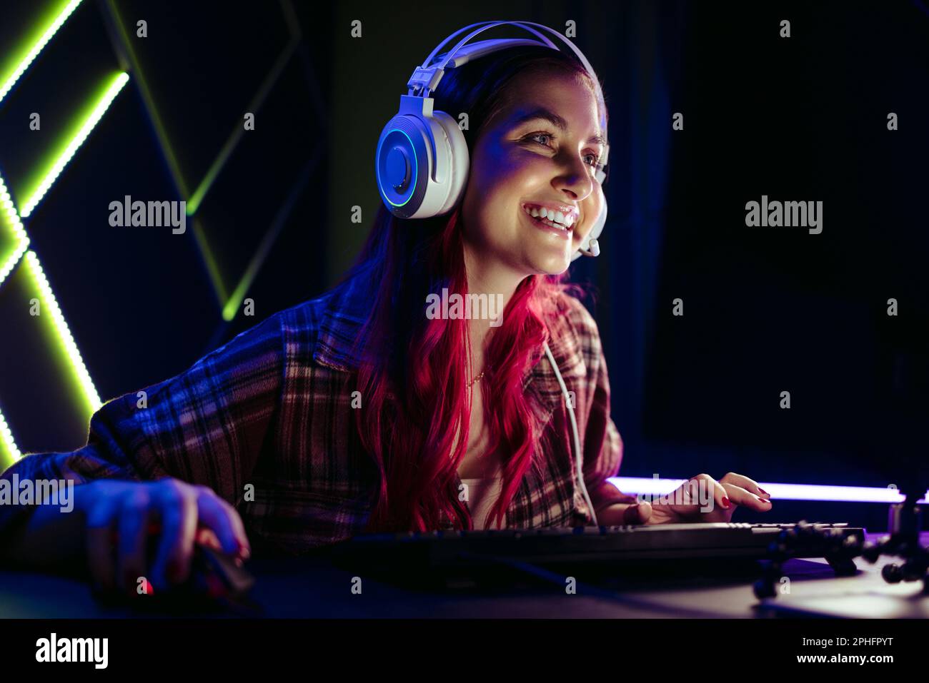 Glückliche Gamer-Frau lächelt auf ihren Computerbildschirm, während sie nachts ein Singleplayer-Videospiel spielt. Ein engagierter Videospielspieler, der sich wie ein Sch amüsiert Stockfoto