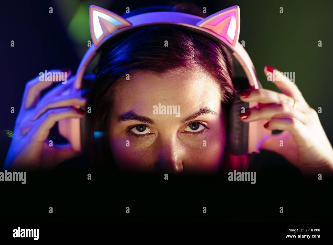 Ein Mädchen, das sein Headset aufsetzt und sich nachts auf ein Online-Videospiel vorbereitet. Weibliche Gamer, die sich in die Welt der E-Sport einmischen, sitzen vor einem Stockfoto
