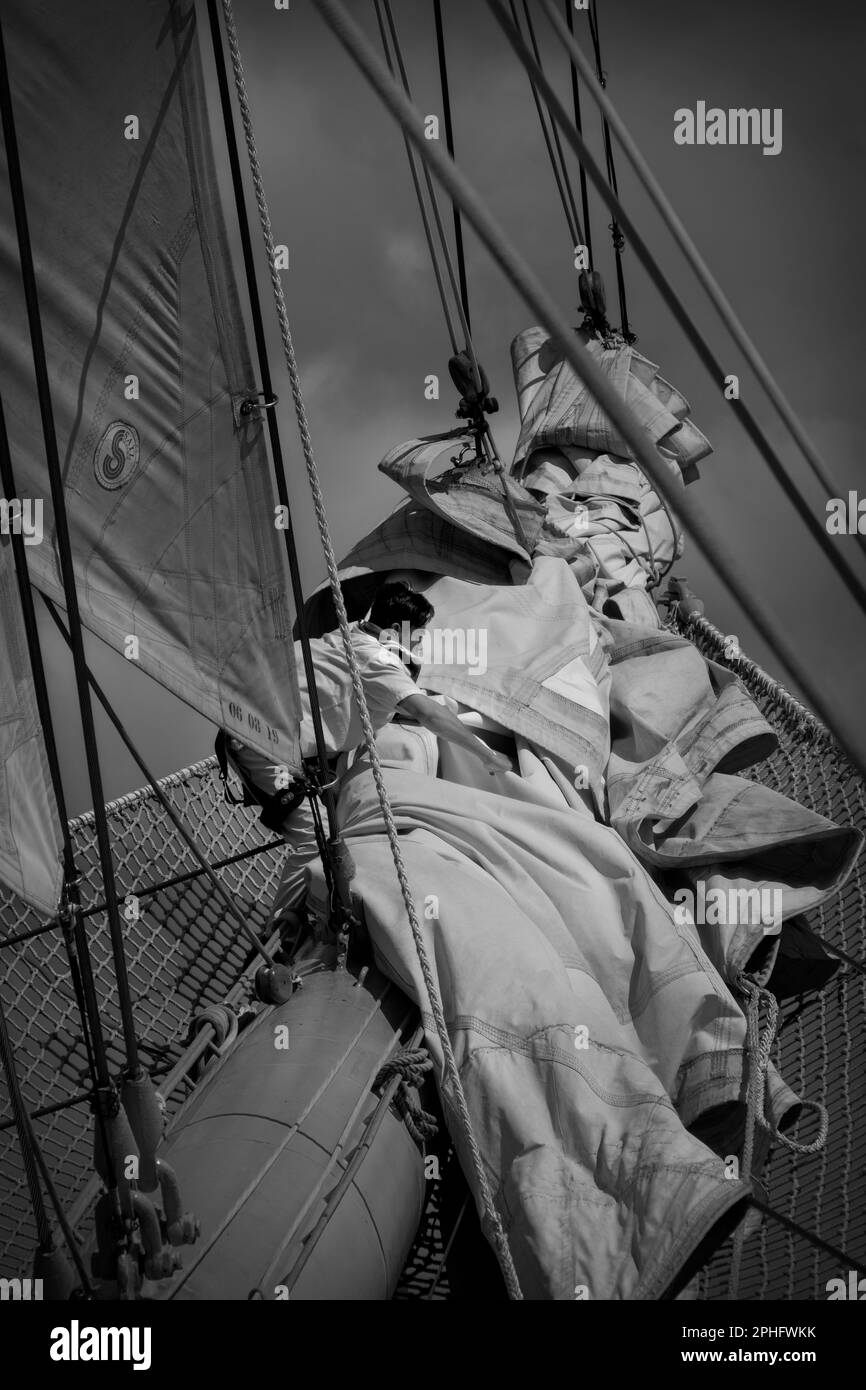 15Feb2023 Barbados Caribbean Crewman von Royal Clipper, der Segel auf einem Jib-Boom mit Sicherheitsnetz auf See während einer Bootstour in Schwarzweiß behandelt Stockfoto