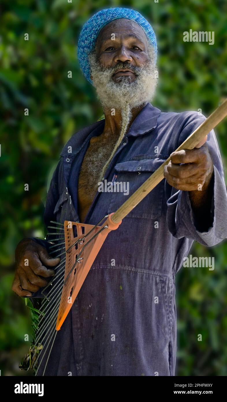 15Feb2023 Barbados Caribbean Gardener posiert für ein spontanes Touristenfoto mit seinem Rake als Gitarre. Lokaler Charakter mit Sinn für Humor. Stockfoto