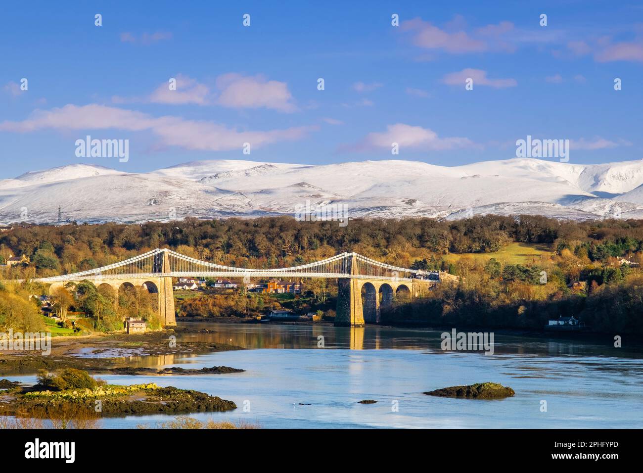 Malerischer Blick auf die Menai-Hängebrücke, die die Menai-Straße überquert, mit Schnee auf den Bergen im Winter. Menai Bridge, Isle of Anglesey, Wales, Vereinigtes Königreich Stockfoto