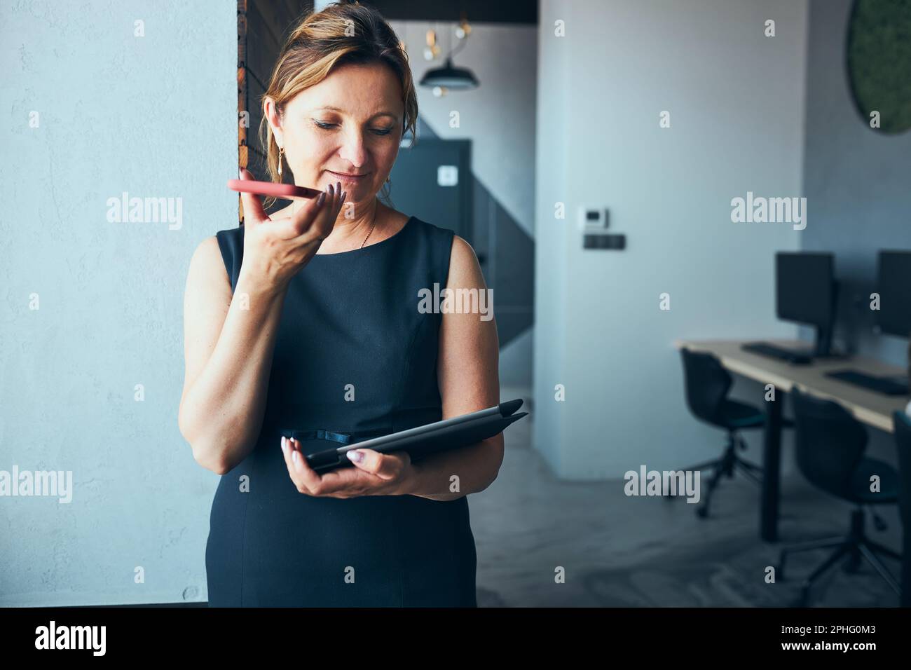 Geschäftsfrau mit Geschäftsanruf, die im Büro am Tablet arbeitet. Reife beschäftigte Frau mit Touchpad-Computer, der am Fenster in einem modernen Interieur steht. Fema Stockfoto