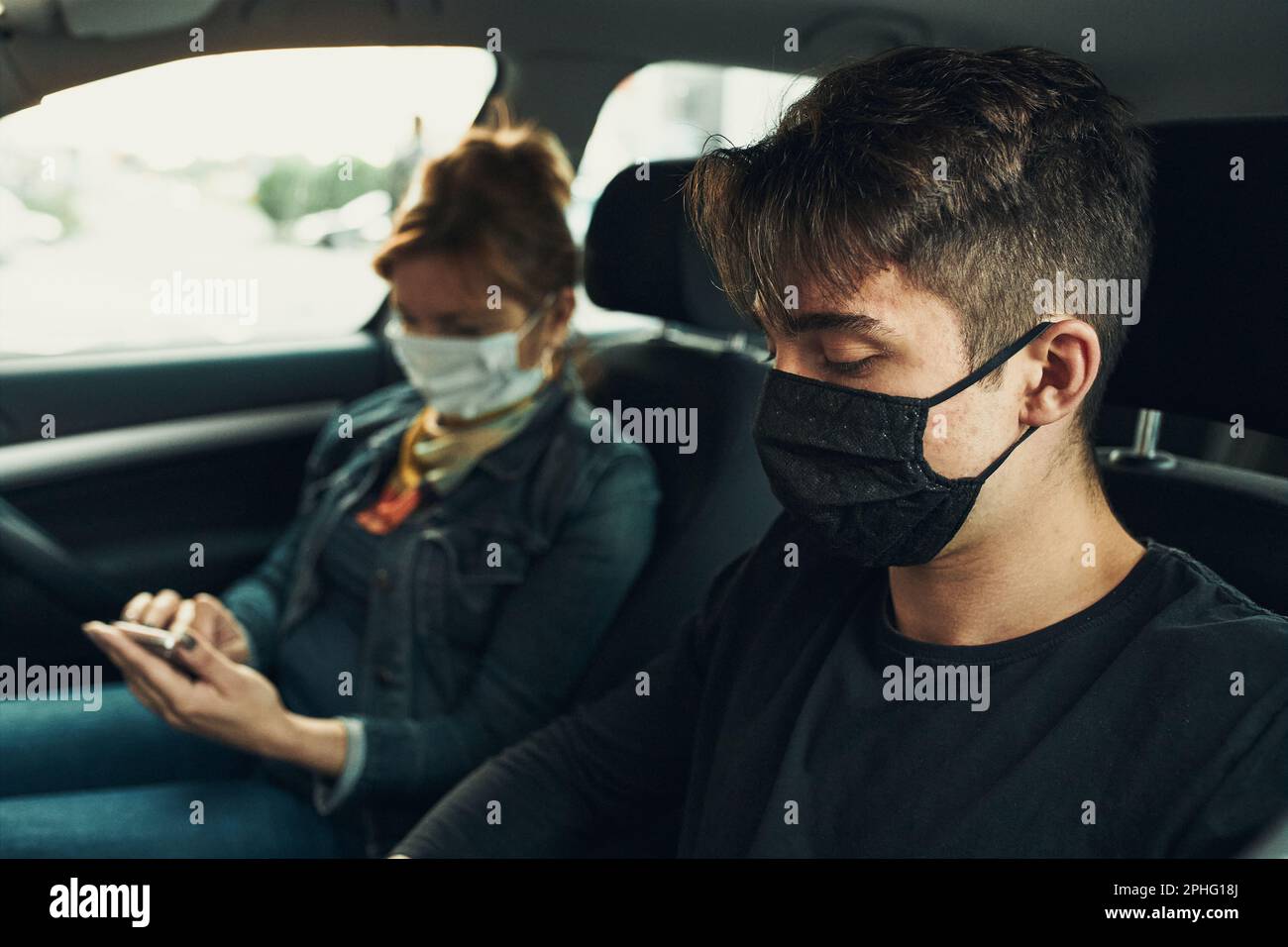 Mann und Frau sitzen in einem Auto mit Smartphones tragen die Gesichtsmasken, um Virusinfektion zu vermeiden und die Ausbreitung der Krankheit in der Zeit von coron zu verhindern Stockfoto