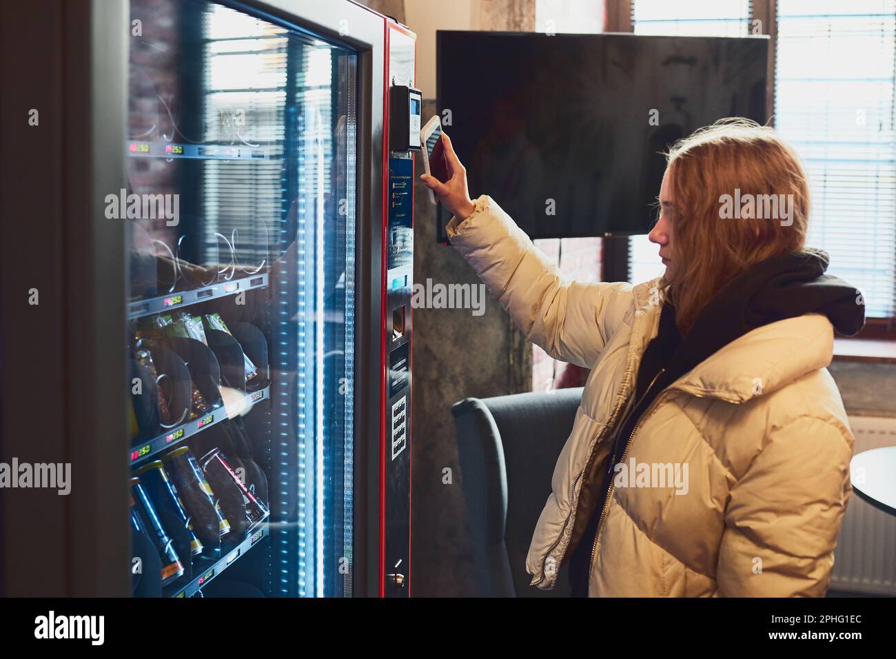 Frau, die für das Produkt am Verkaufsautomaten mit kontaktloser Zahlungsmethode mit dem Mobiltelefon bezahlt. Frau nutzt neue Zahlungsmittel Stockfoto