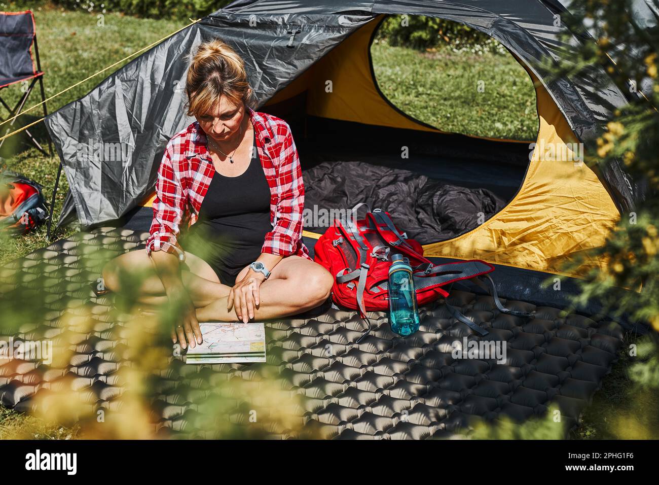 Frau, die die nächste Reise plant, während sie mit Karte im Zelt sitzt. Frau, die sich im Zelt während der Sommerferien beim Camping entspannt. Verbringen Sie aktiv Urlaub im Freien Stockfoto