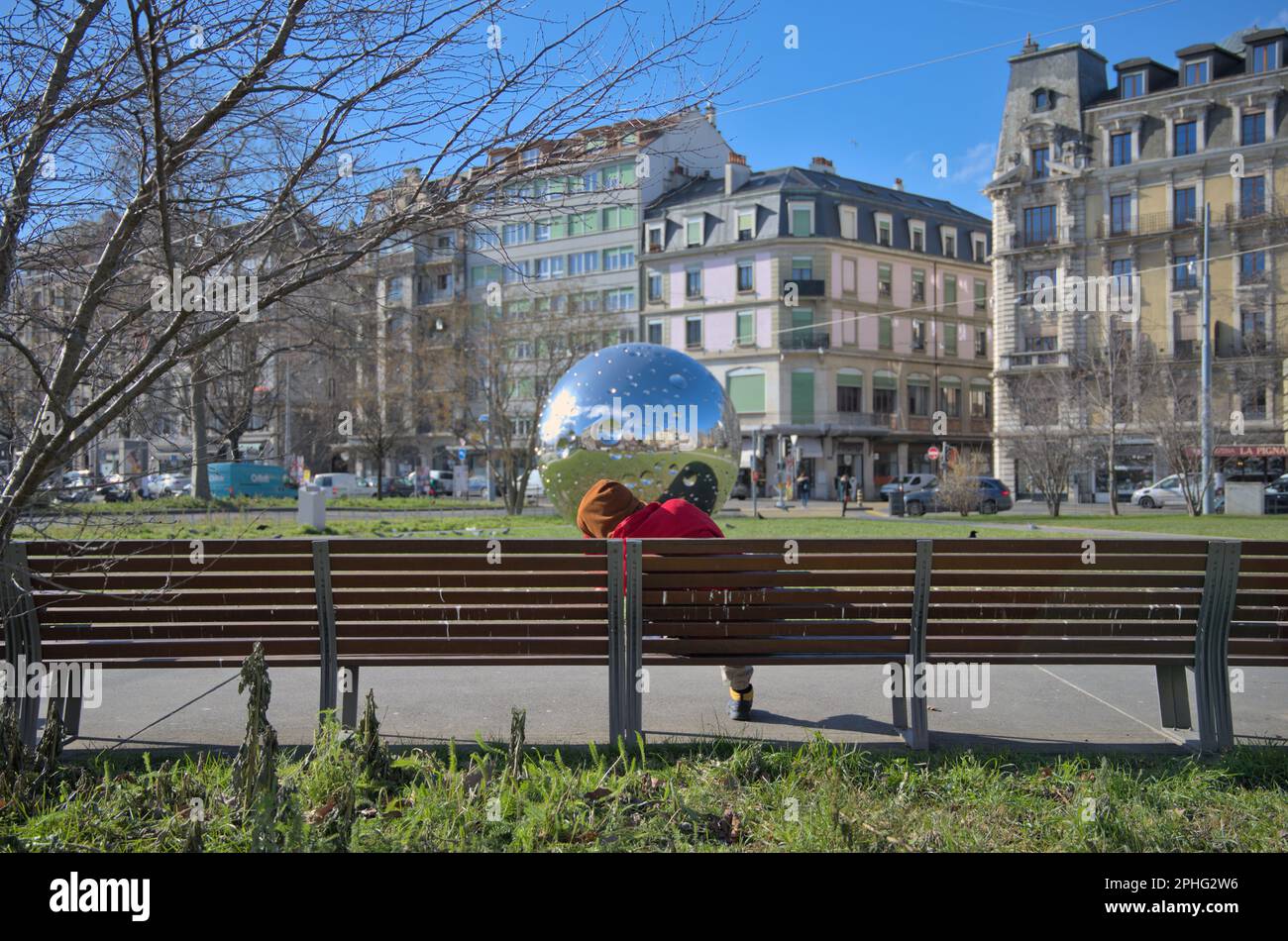 Tagsüber eingeschlafene Person auf einer Bank mit der Spiegelkugel von Plainpalais im Hintergrund Stockfoto