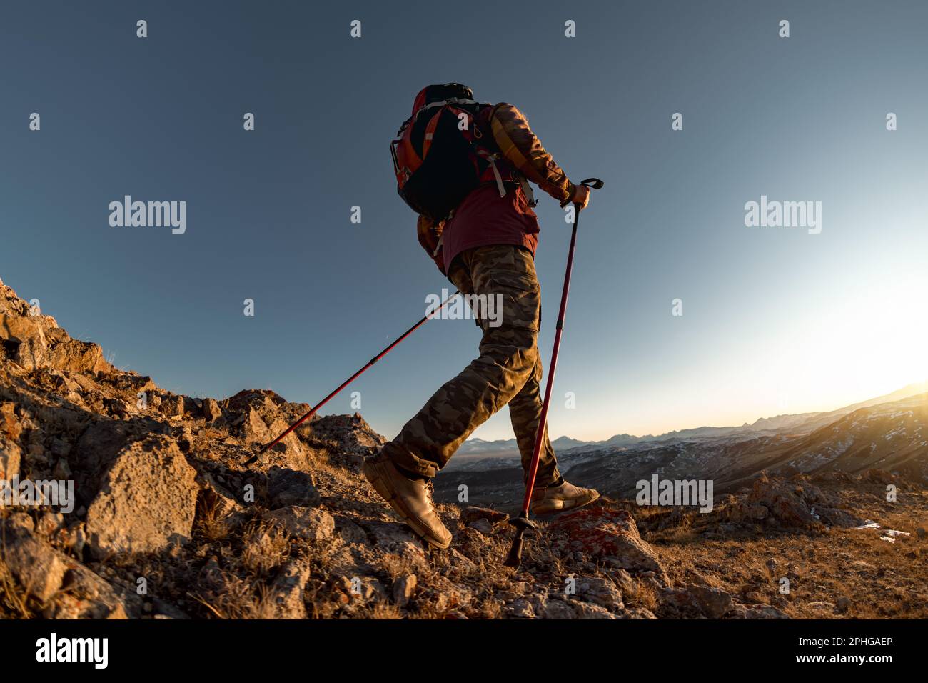 Wanderer mit Rucksack wandern bergauf in den Bergen. Die aktive Tourismussilhouette passt zu Wanderstöcken bei Sonnenuntergang Stockfoto