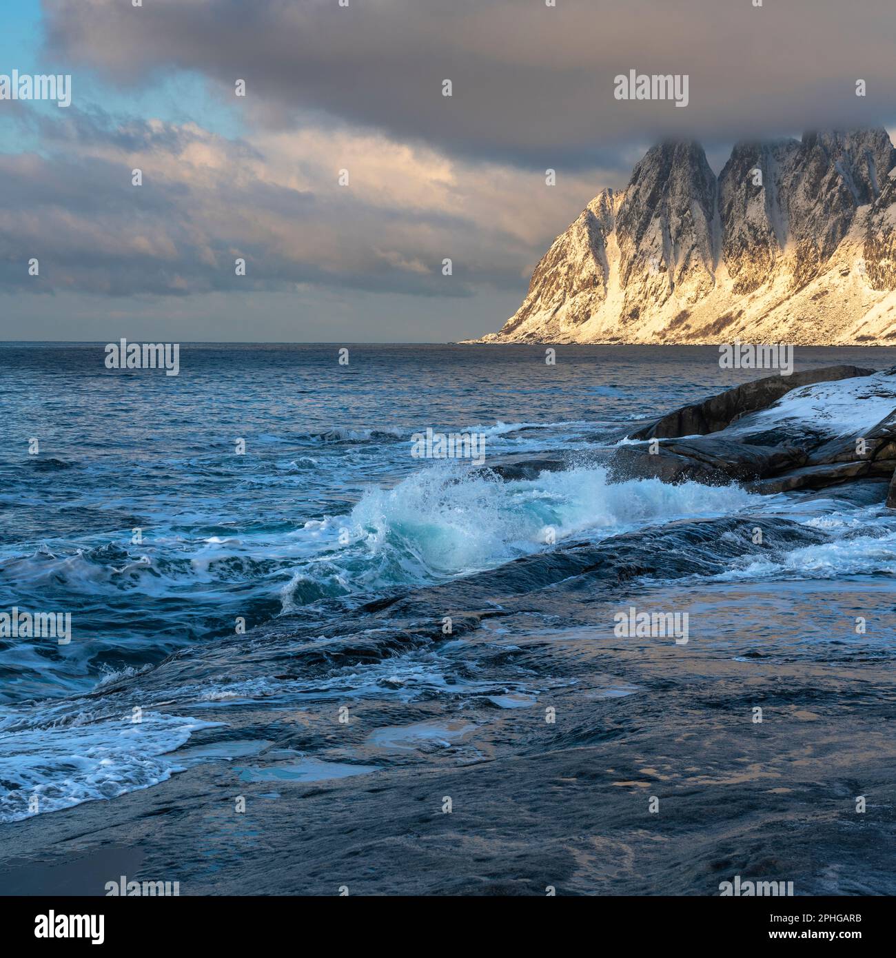 Am Fels sich brechende Wellen des Atlantik bei Tungeneset, Senja, Norwegen, mit den steilen Bergen Okshornan im Hintergrund. Stürmisches Winterwetter Stockfoto