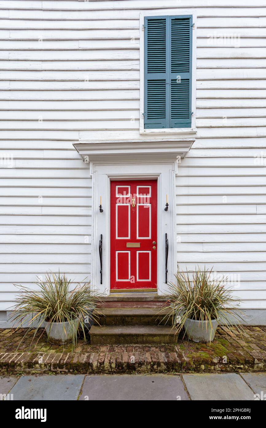 Hellrote Eingangstür unter einem blauen Fensterläden auf einem weißen Klappbrettgebäude Stockfoto