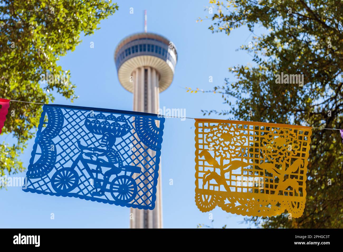 Blauer und gelber Papel picado bei der Todestag-Feier in San Antonio, Texas, mit dem Tower of the Americas im Hintergrund Stockfoto