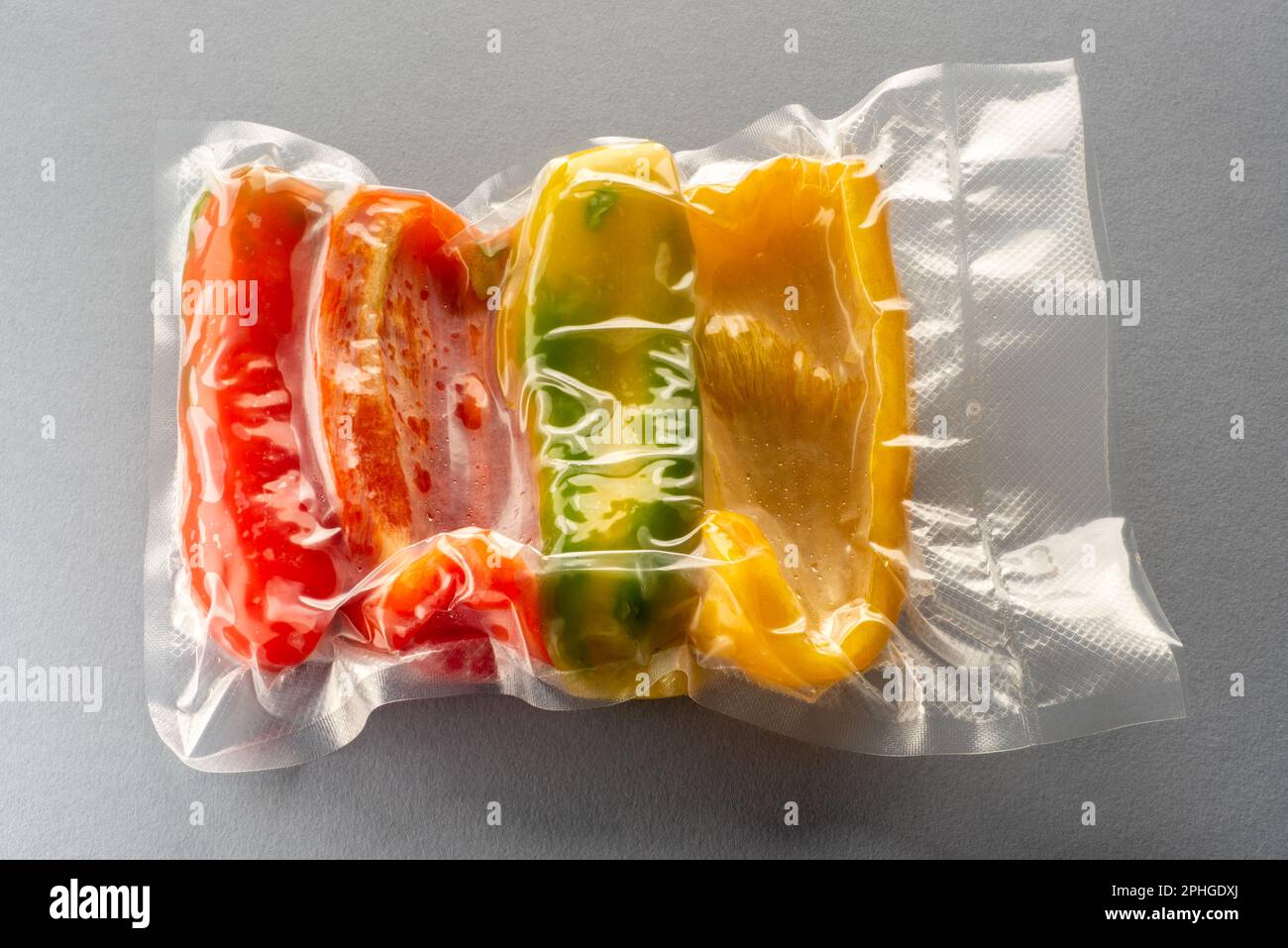 Scheiben gelber roter und grüner Paprika in vakuumversiegelter Verpackung für Sous Vide Kochen auf ionengrauem Hintergrund Stockfoto