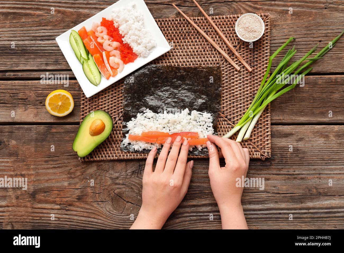 Frau, die Sushi-Brötchen auf Holzhintergrund zubereitet Stockfoto