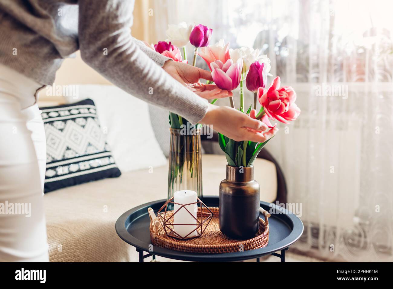 Frau genießt Tulpen Blumen in Vasen auf Tisch mit Tablett und Kerze gesetzt. Gemütliches Interieur und Frühlingsdekor zu Hause Stockfoto