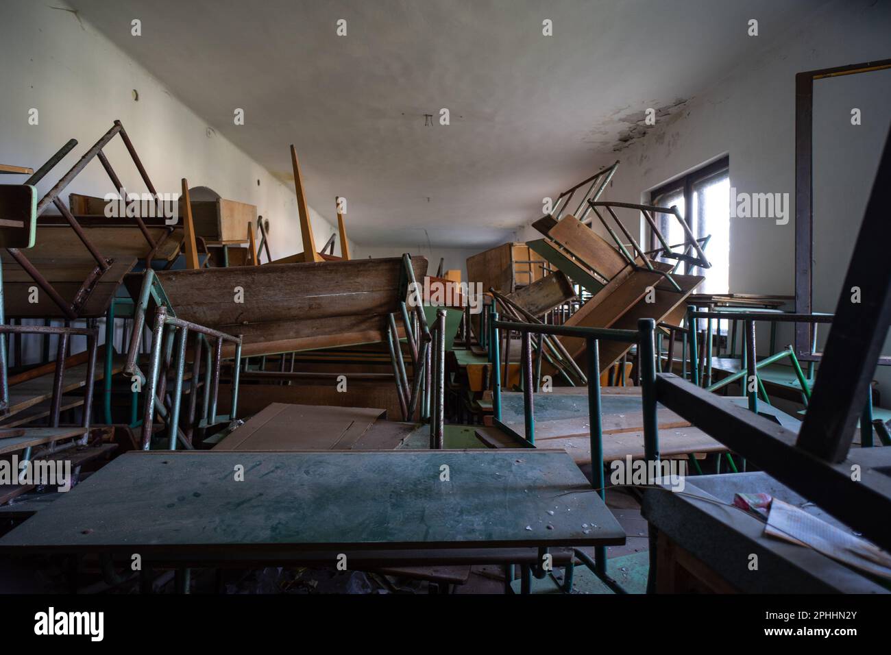 Verstreute und umgestürzte Schreibtische in einem verlassenen Klassenzimmer Stockfoto