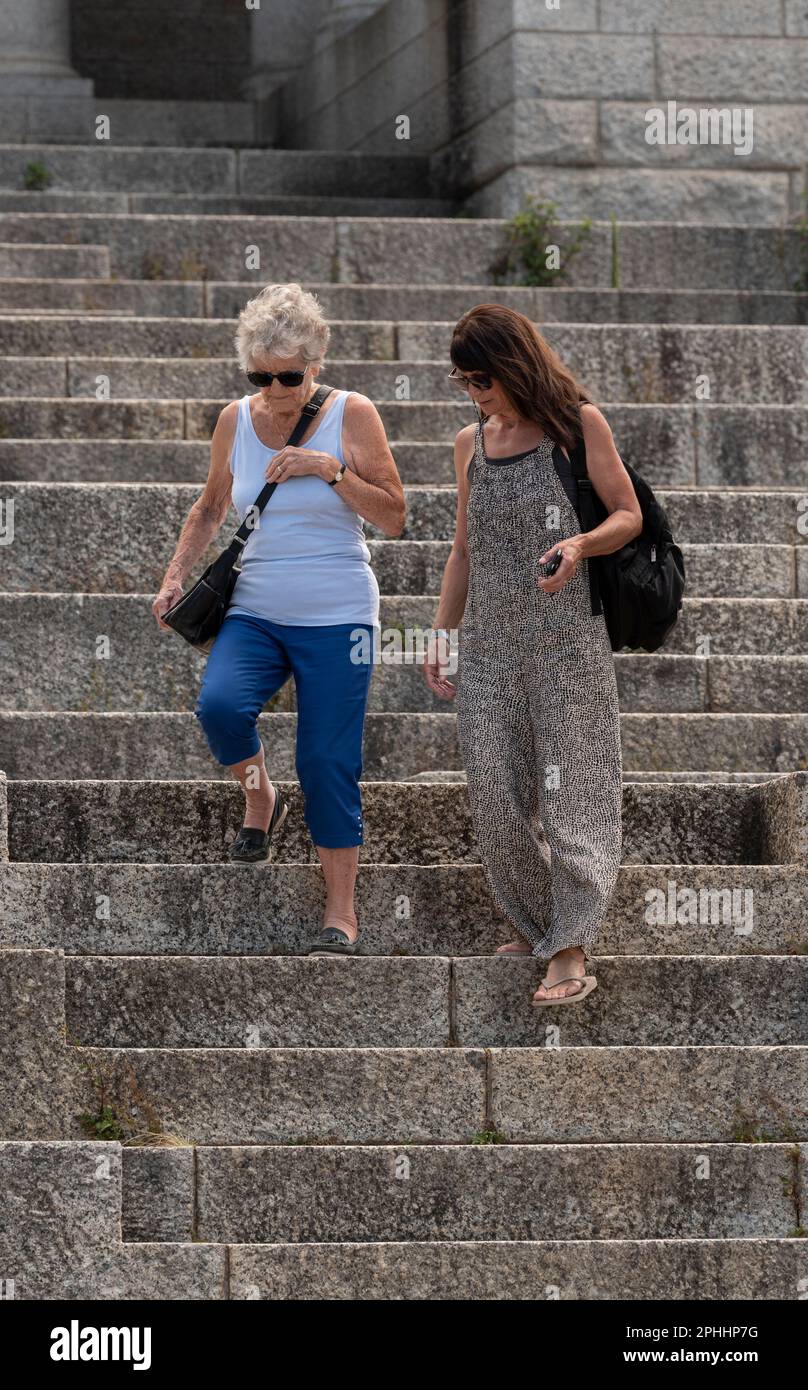 Kapstadt, Südafrika. 2023. Ältere Menschen, die Hilfe von einer Betreuerin erhalten, wenn sie sehr steile Treppen bei einer Touristenattraktion hinuntergehen. Stockfoto