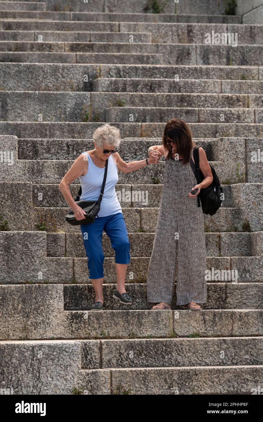 Kapstadt, Südafrika. 2023. Ältere Menschen, die Hilfe von einer Betreuerin erhalten, wenn sie sehr steile Treppen bei einer Touristenattraktion hinuntergehen. Stockfoto