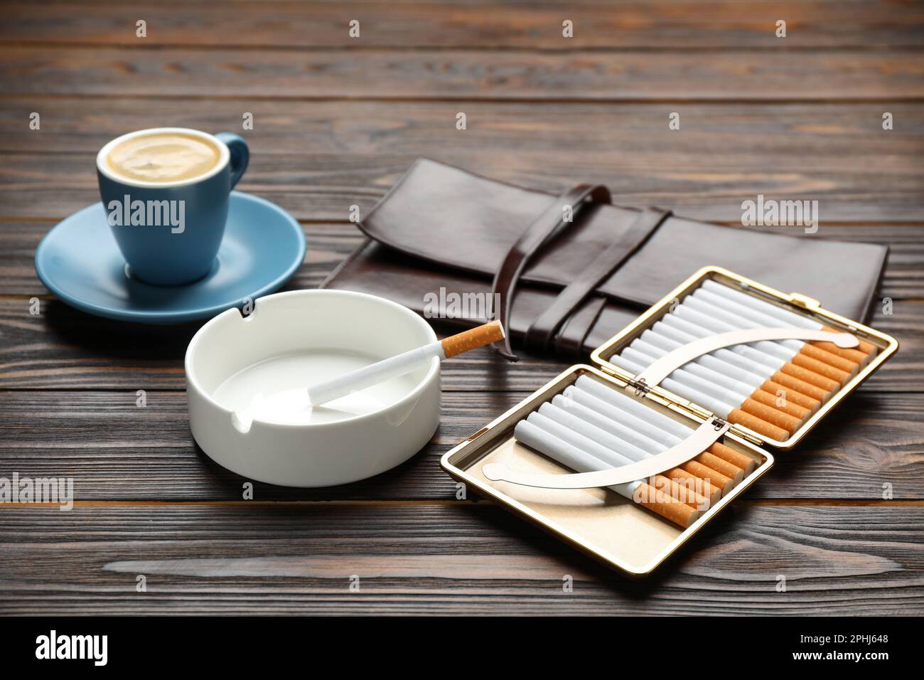 Offener Koffer mit Tabakfilterzigaretten, Aschenbecher, Kupplung und Tasse Kaffee auf Holztisch, Nahaufnahme Stockfoto