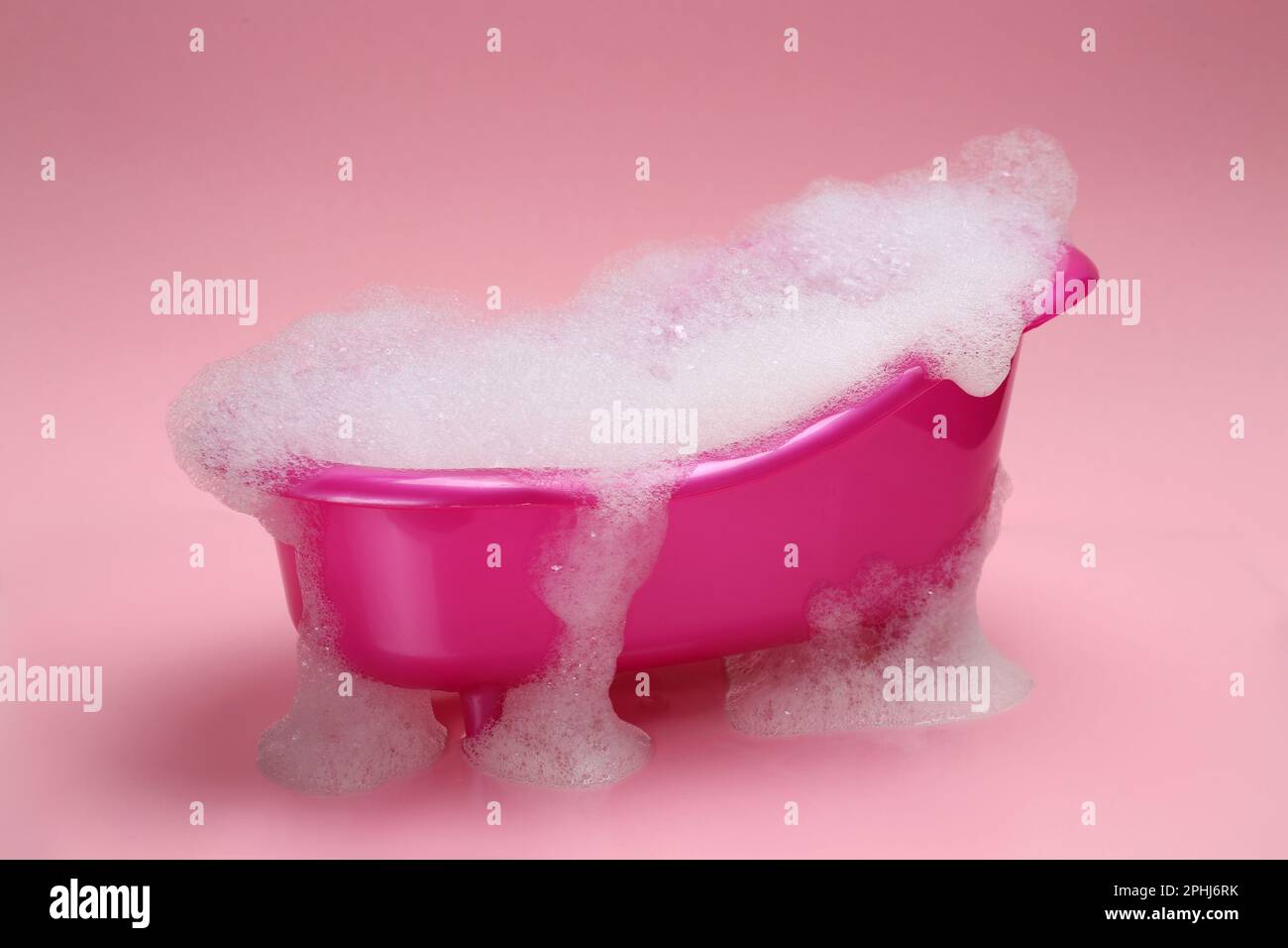 Spielzeugbadewanne mit Schaumstoff auf pinkfarbenem Hintergrund Stockfoto
