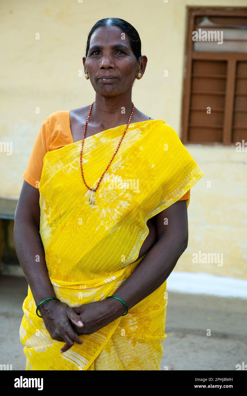 Eine Frau mit gelbem Sari, die sich in einem ländlichen indischen Dorf posiert Stockfoto
