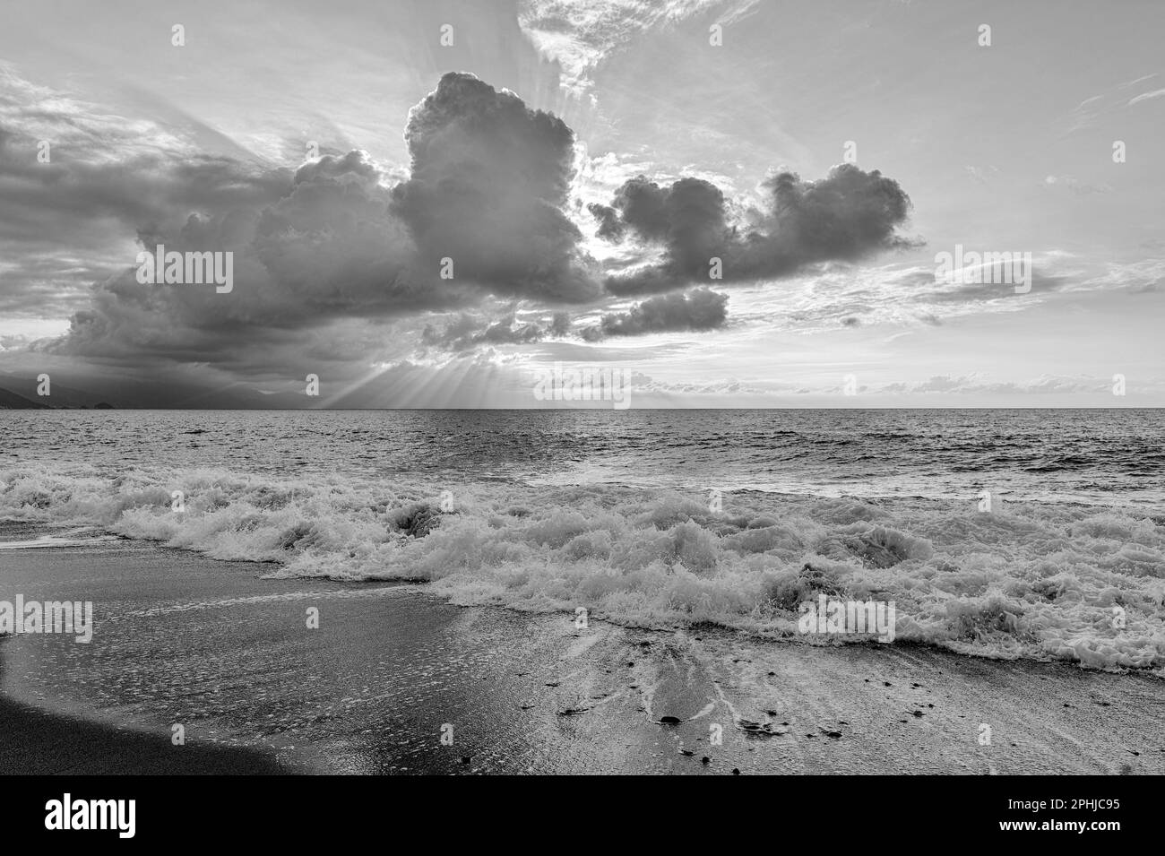 Ein Sonnenuntergang Am Meer Mit Sonnenstrahlen, Die Hinter Den Wolken Schwarz Und Weiß Ausstrahlen Stockfoto