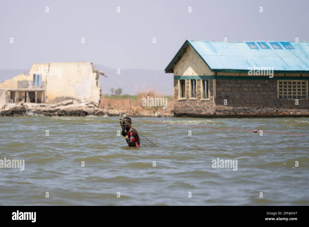 Kalokol, Kenia. 14. Februar 2023. Ein Kalokol-Fischer, der mit seinem Netz im Turkana-See spaziert. Das Dorf Kalokol ist in den letzten Jahren überflutet worden, weil der Turkana-See und alle anderen Seen des Rift Valley aufgrund des Klimawandels enorm angestiegen sind. Dieses Phänomen hat ganze Dörfer überschwemmt, die Bevölkerung gezwungen, ihre Häuser und Geschäfte aufzugeben, und hat verheerende Auswirkungen auf die natürlichen Ökosysteme. (Kreditbild: © Simone Boccaccio/SOPA Images via ZUMA Press Wire) NUR REDAKTIONELLE VERWENDUNG! Nicht für den kommerziellen GEBRAUCH! Stockfoto