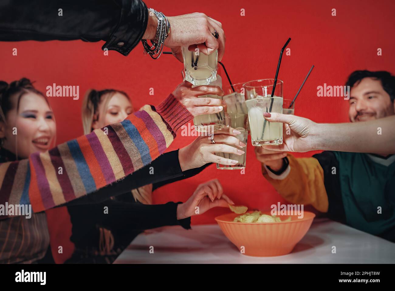 Eine vielfältige Gruppe von Freunden, die mit erhöhten Gläsern in einem Pub mit roter Wand anstoßen, konzentriert sich auf Gläser, kaukasische und asiatische Personen. Stockfoto