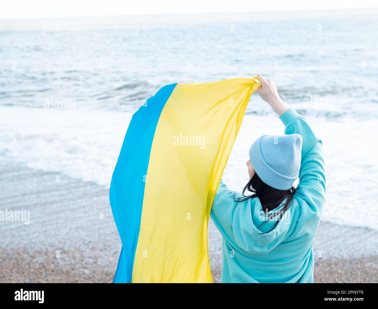 Braune Frau in blauem Hoodie und blauem Hut mit ukrainischer Nationalflagge Stockfoto