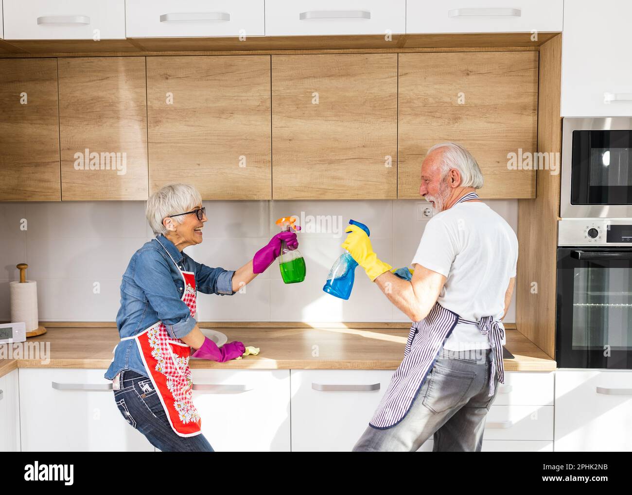 Reifes Paar, das in der Küche Hausarbeiten macht, mit Sprühflaschen spielt und Spaß hat Stockfoto