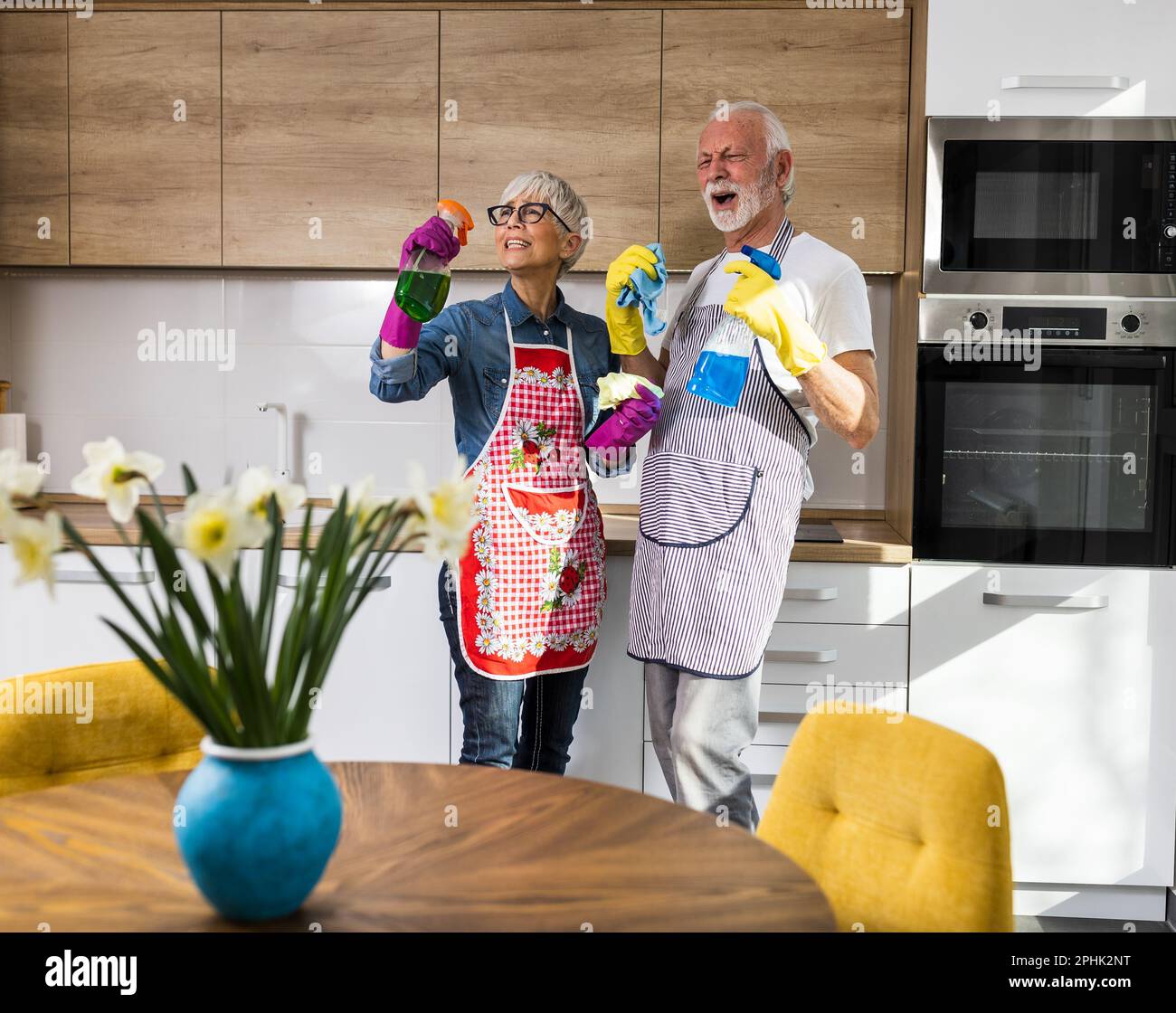 Reifes Paar, das Spaß hat, während es in der Küche arbeitet und auf Sprühflaschen singt Stockfoto