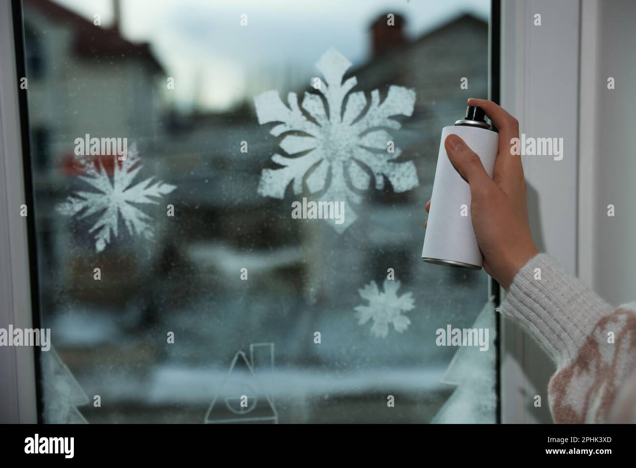 Eine Frau, die zu Hause Schneespray benutzt, um Fenster mit Schneeflocken  zu dekorieren, Nahaufnahme Stockfotografie - Alamy