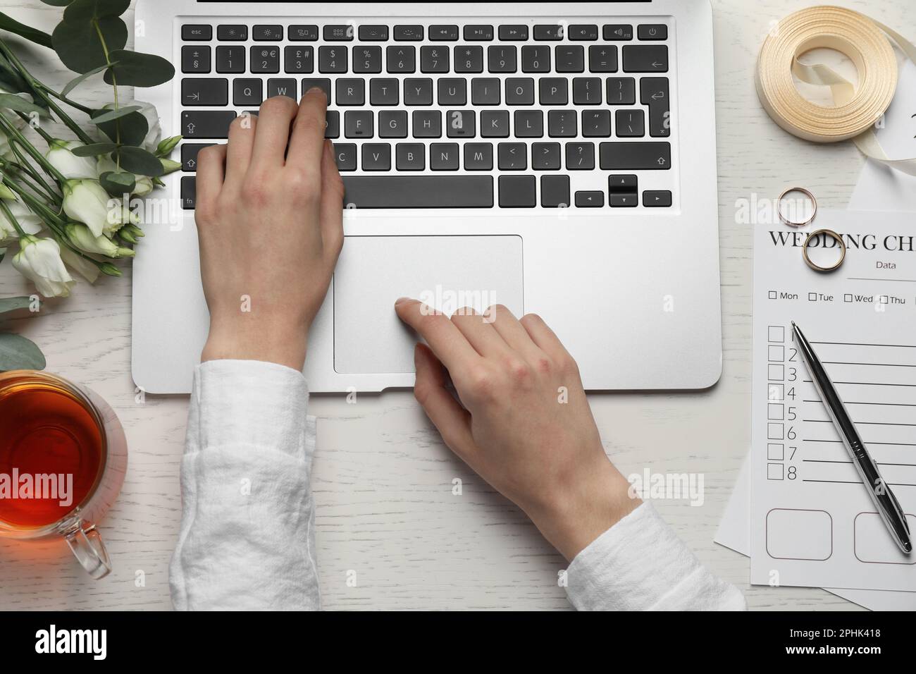 Frau mit Laptop und Hochzeits-Checkliste am weißen Holztisch, Draufsicht Stockfoto