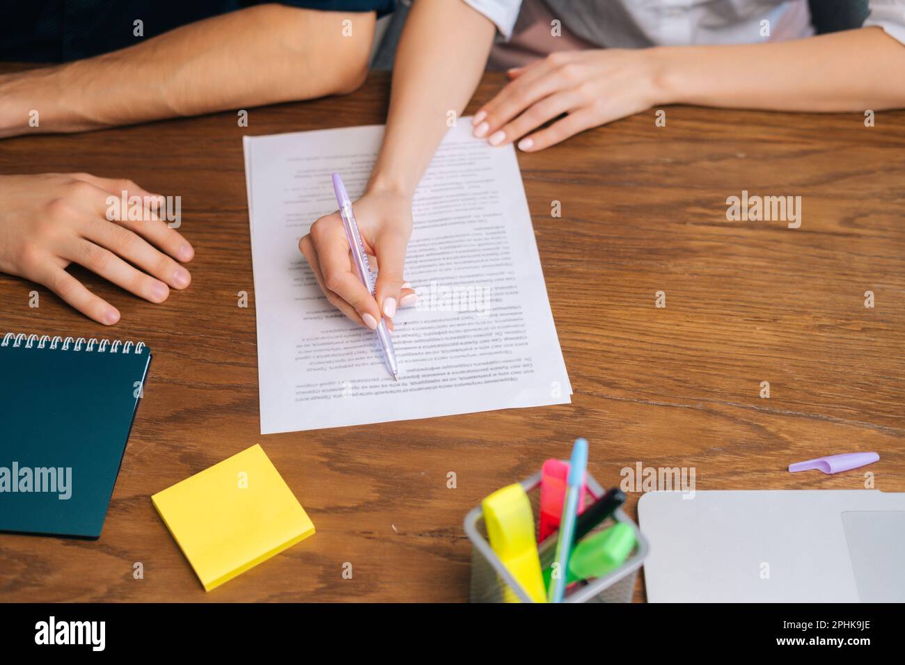 Nahaufnahme aus dem Blickwinkel einer unbekannten Geschäftsfrau, die einen Vertrag oder eine Vereinbarung am Tisch im Büro liest und unterschreibt. Stockfoto