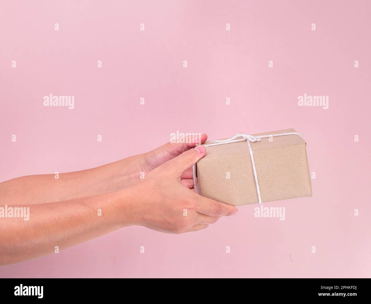 Nahaufnahme einer weiblichen Hand, die Geschenkbox oder Geschenkbox in Kunsthandwerk auf pinkfarbenem Hintergrund hält. Kleines Geschenk in weiblichen Händen drinnen. Stockfoto
