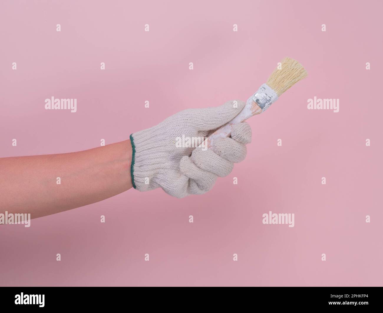 Hand in weißem Strickhandschuh mit Farbpinsel isoliert auf pinkfarbenem Hintergrund. Stockfoto