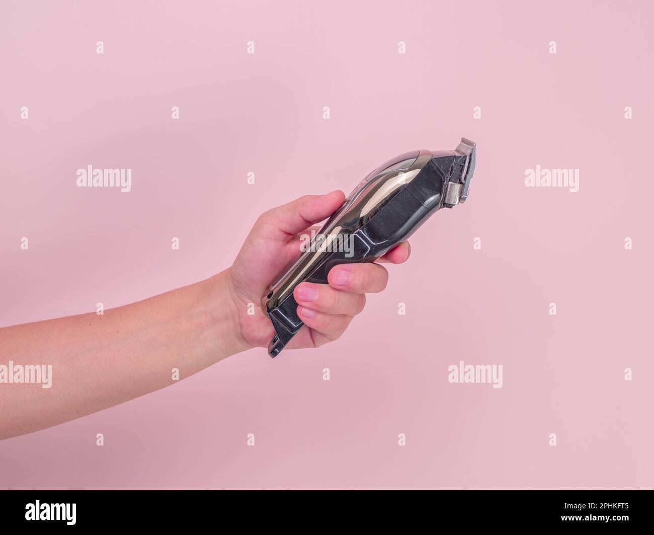 Nahaufnahme Hand mit elektrischem Haarschneider auf pinkfarbenem Hintergrund. Haarschneidemaschine in der Hand. Stockfoto