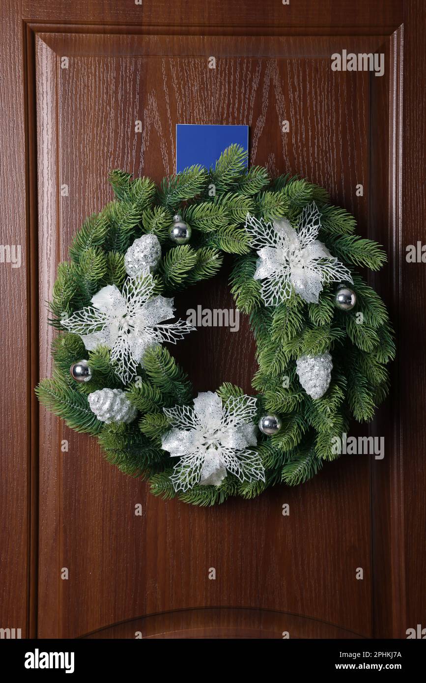 Wunderschöner Weihnachtskranz mit festlichem Dekor, das an einer Holztür hängt Stockfoto