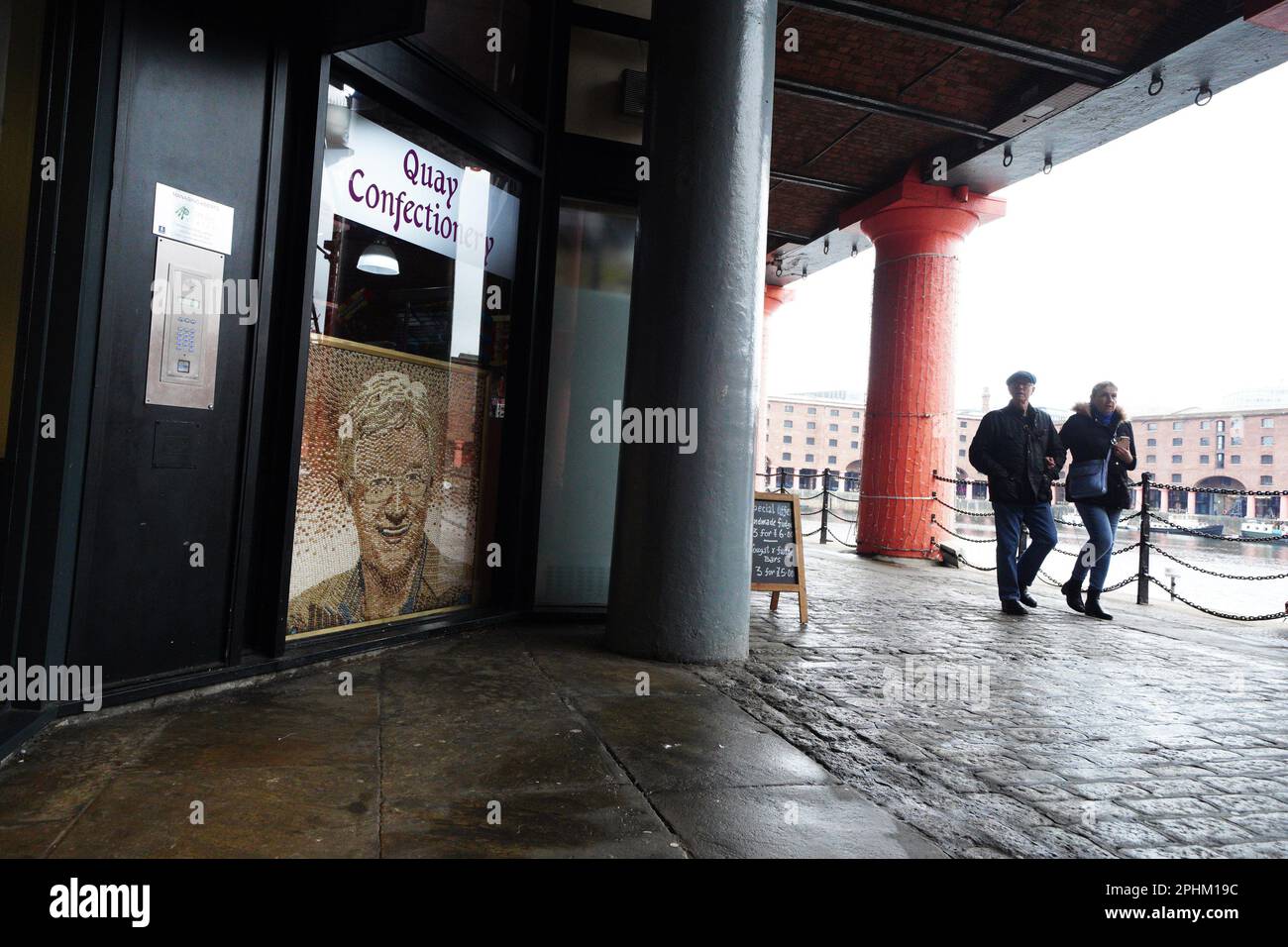 Die Leute gehen an einem Porträt von Paul O'Grady vorbei, das aus Geleebohnen hergestellt wurde und im Quay Confectionary in Liverpools Albert Docks ausgestellt ist, während der Fernsehmoderator und Komiker im Alter von 67 Jahren gestorben ist, sagte sein Partner Andre Portasio. Bilddatum: Mittwoch, 29. März 2023. Stockfoto