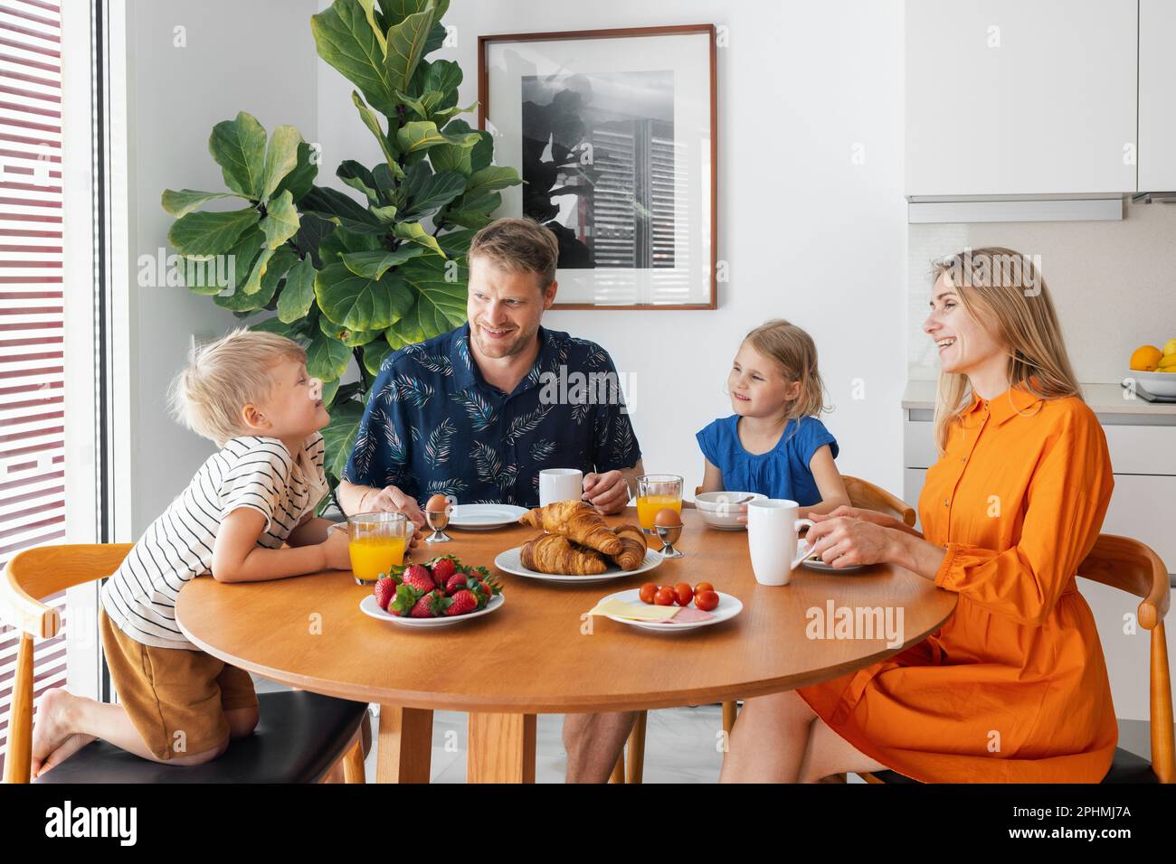 Glückliche Familie mit zwei Kindern, die am Tisch sitzen und morgens in der Küche frühstücken Stockfoto
