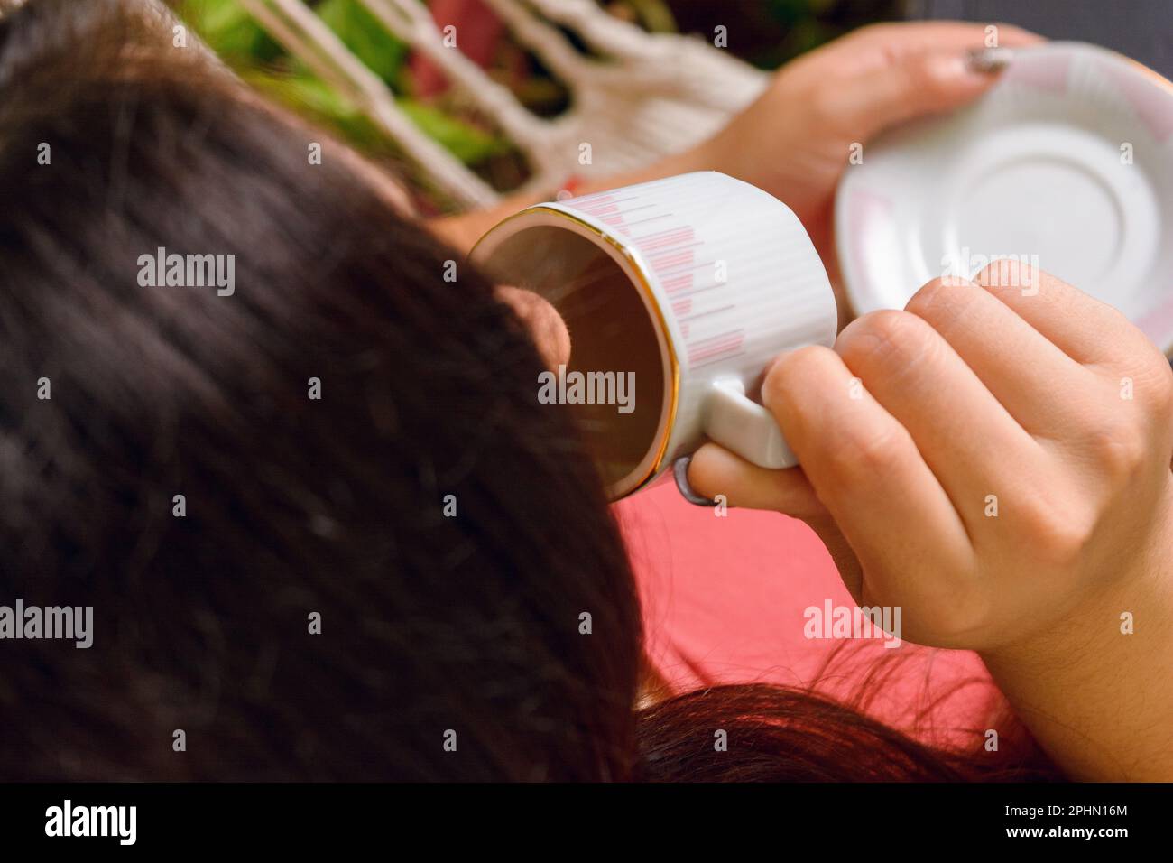 Rückansicht von oben, von einer nicht wiedererkennbaren, weiß gehäuteten Frau, die zu Hause sitzt und Kaffee in einer kleinen Tasse trinkt. Stockfoto