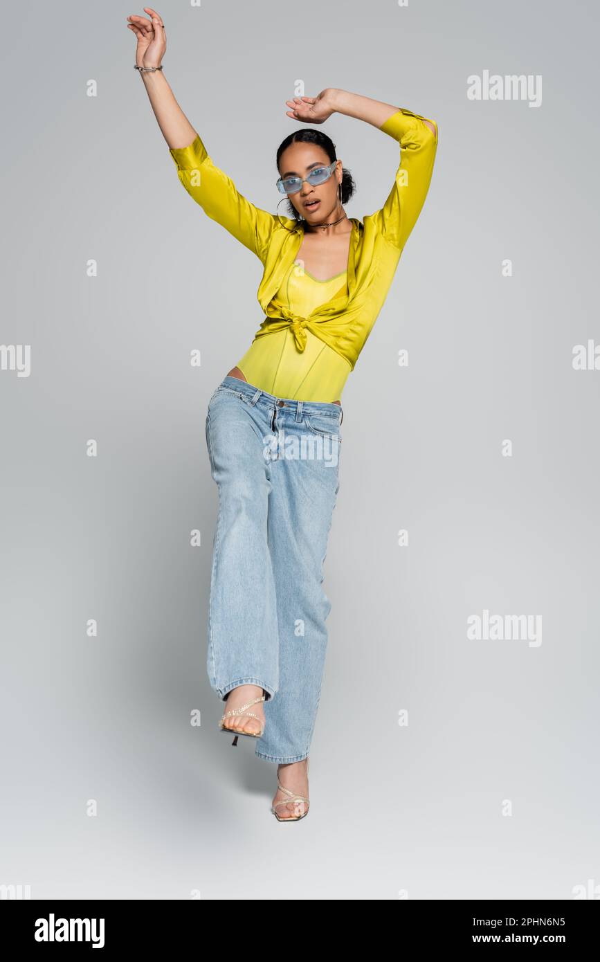 Ein überraschtes afroamerikanisches Model in trendigen Kleidern, das auf einem Bein auf einem grauen Stockbild posiert Stockfoto