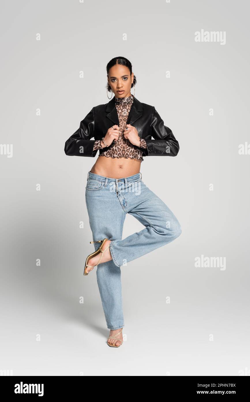 Ein elegantes afroamerikanisches Modell in verkürzter Jacke und Jeans, das auf einer LED posiert und auf einem grauen Stock-Bild steht Stockfoto